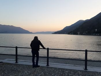 Silhouette man standing on railing by sea against sky during sunset