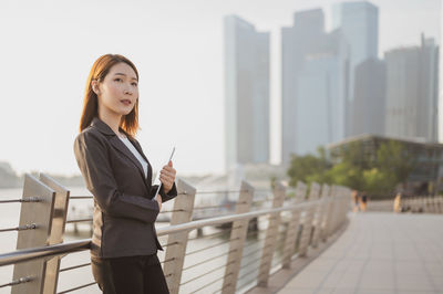 Portrait of young woman standing against railing in city