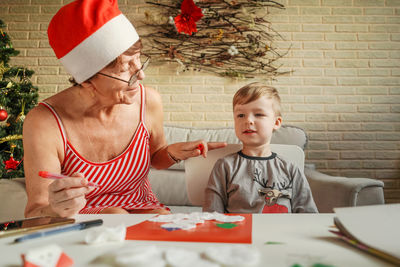 Senior woman with grandson making greeting card on table at home