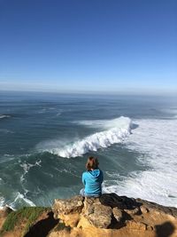 Rear view of woman sitting on rock by sea against sky