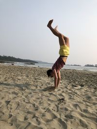 Woman with arms raised on beach against clear sky