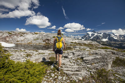 Rear view of female hiker with backpack by pond against mountains and cloudy sky during winter at north cascades national park