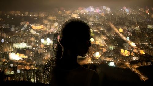 Silhouette woman looking at illuminated cityscape at night