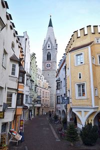 Street amidst old buildings leading towards clock tower in town against clear sky