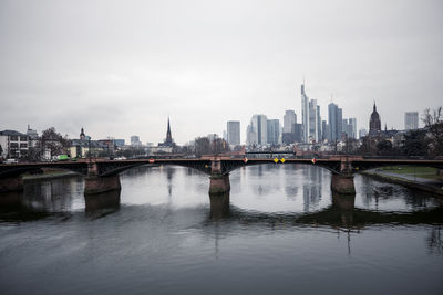 Bridge over river by buildings against sky in city