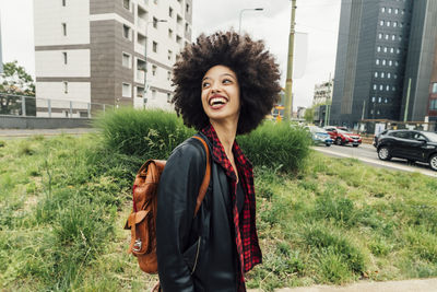 Happy woman with backpack looking back over shoulder in city