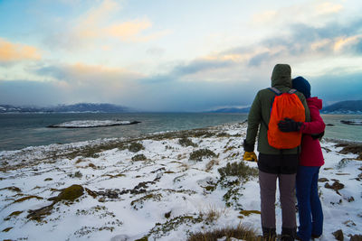 Couple looking at sea while standing on snow covered land