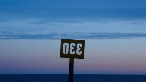Upside down signboard on sea shore during sunset