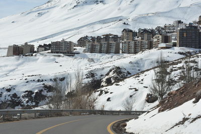 Snow covered road by buildings in city