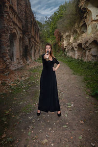 Young woman points a gun at the camera against the background of the ruins of the fortress.