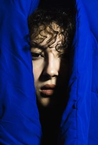 Close-up portrait of young woman looking through curtain