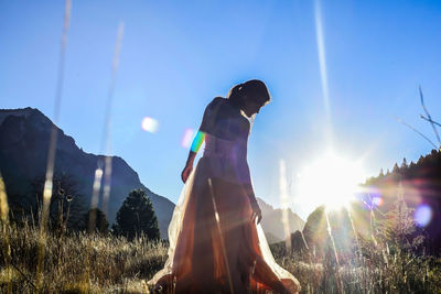 Woman standing on field against sky on sunny day