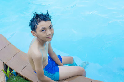 Portrait of boy sitting by swimming pool