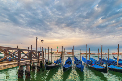 Boats moored in canal against cloudy sky