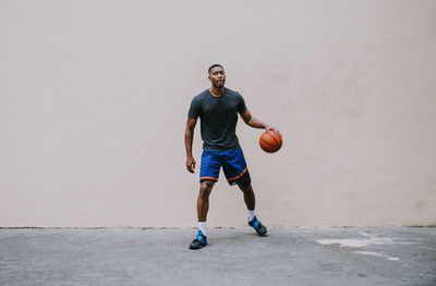 Full length portrait of young man playing basketball against wall
