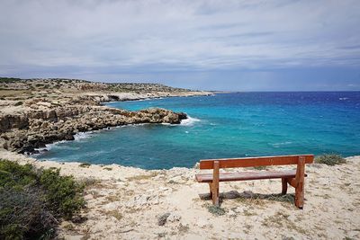 Empty bench on shore by sea against sky