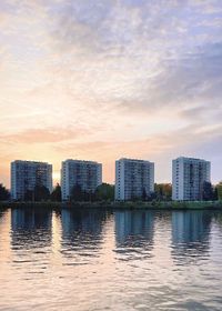 Scenic view of lake by buildings against sky during sunset