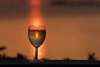 Close-up of wineglass on table against orange sky