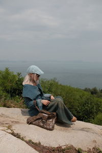 Rear view of woman sitting on rock against sky
