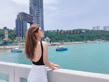 Woman standing by swimming pool in city against sky