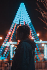 Woman standing against illuminated lighting equipment at night