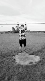 Full length of boy hanging from metallic rod on field against sky