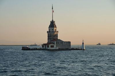 Lighthouse by sea against clear sky during sunset