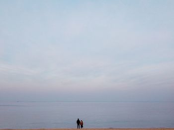 Rear view of friends standing at beach against sky