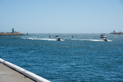 Boats sailing in sea against clear sky