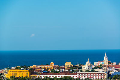 High angle view of city by sea against blue sky