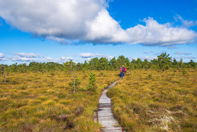 People walking on dirt road amidst field against sky
