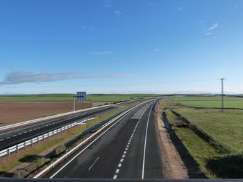 High angle view of empty highway amidst grassy fields against blue sky