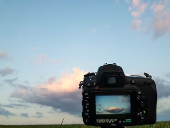 Close-up of camera photographing against sky during sunset