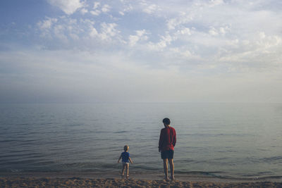 Rear view of people enjoying at beach against sky