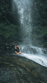 Man sitting against waterfall in forest