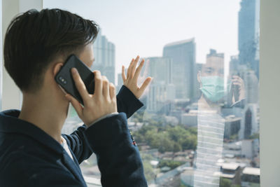 Midsection of man photographing cityscape through window