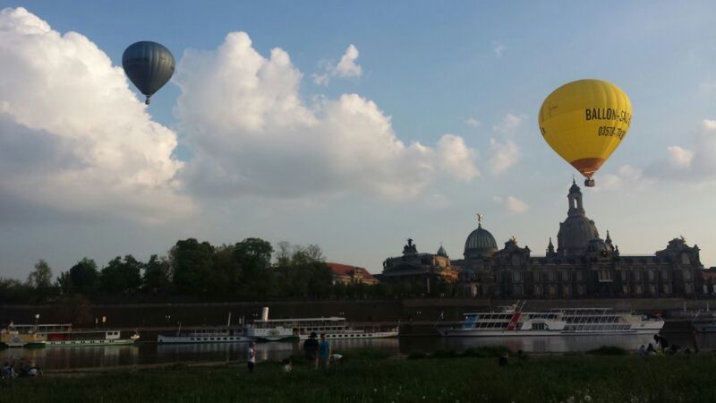 sky, building exterior, built structure, architecture, cloud - sky, flying, mid-air, hot air balloon, transportation, cloud, low angle view, sport, parachute, outdoors, incidental people, landscape, air vehicle, travel, day