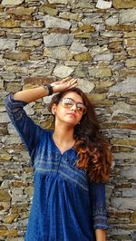 Portrait of young woman standing against brick wall