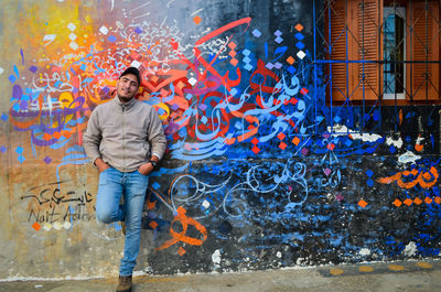 Full length portrait of man standing against graffiti wall