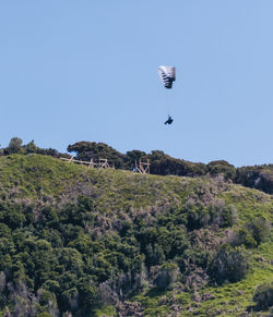 Person paragliding over landscape against clear blue sky