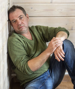 Portrait of depressed mature man sitting on hardwood floor at home