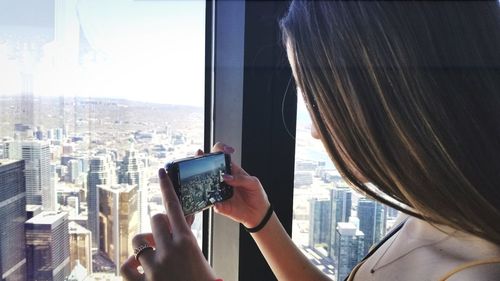 Midsection of man photographing cityscape through window