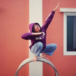 Full length of young woman exercising against orange wall