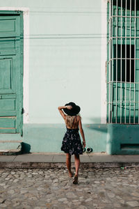 Rear view of woman in hat walking against house