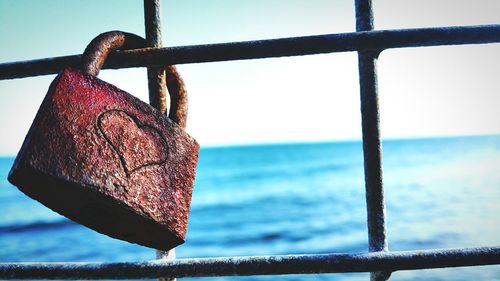 Close-up of padlock attached on fence against sea