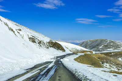 Snow covered road by mountain against blue sky