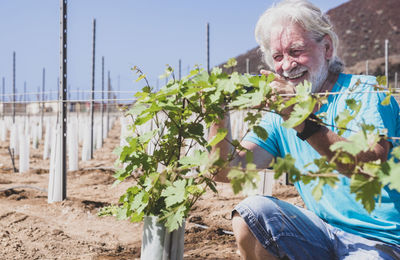 Close-up of smiling senior man crouching by plant outdoors