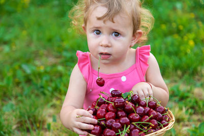 Portrait of cute baby girl with berries sitting on grass