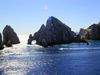 Rocks on sea shore against clear blue sky