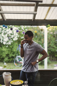 Man using mobile phone while standing in log cabin during party